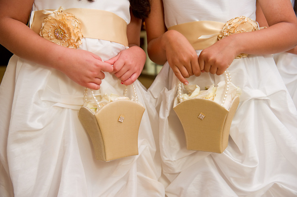 flower girls in beautiful white dresses and golden yellow sash with golden yellow floral design holding golden yellow clutches with pearl straps - photo by Houston based wedding photographer Adam Nyholt